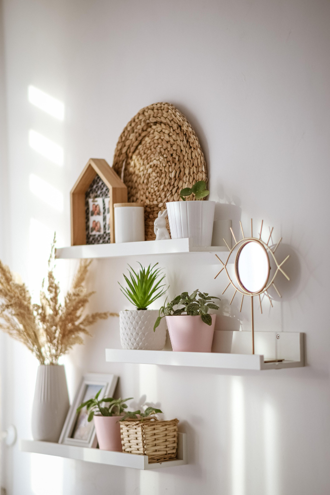 juego de estantes blancos decorados con cuadros y espejos de bordes marrones claros, macetas en color pastel y un espejo con base de madera.
