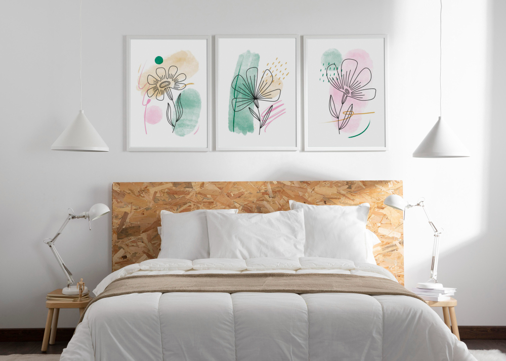 Foto de cama con cubrecama blanco, tres cuadros en colores pastel claro en la pared por encima de la cama y dos banquillos como mesas de noche con sus lámparas blancas estilo escritorio