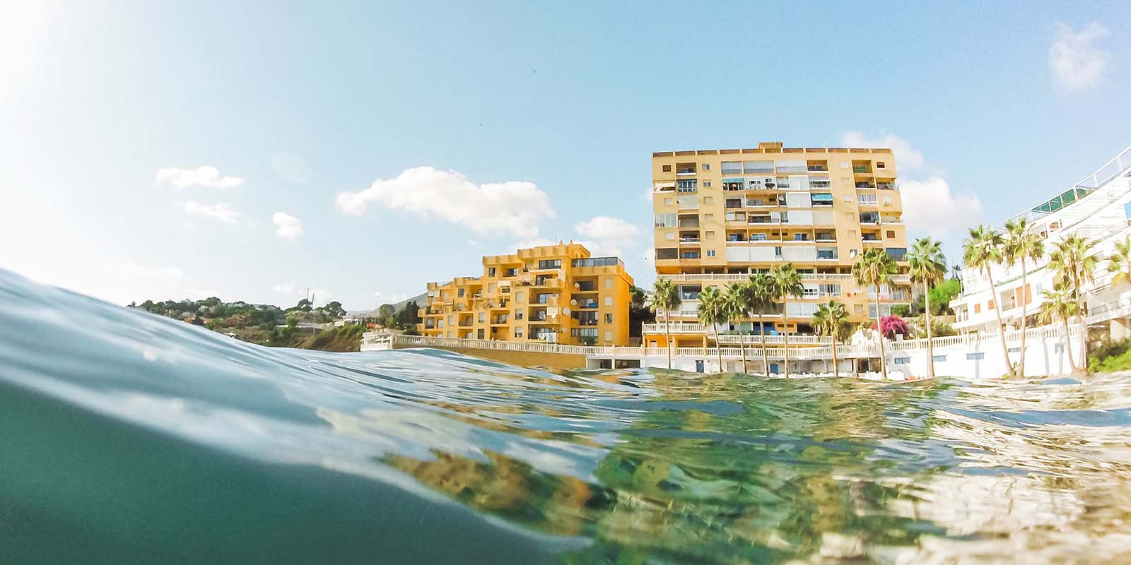 Primer plano de una ola baja de océano con un edifico de fondo. Gisela Juarez puede ayudarte a encontrar un piso para alquilar.