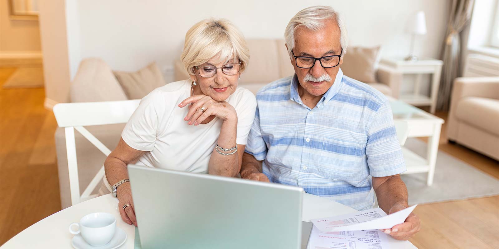 Pareja adultos mayores sentados en una mesa con el portátil y documentación. En concepto de conocer las posibles exenciones a la hora de vender su vivienda.