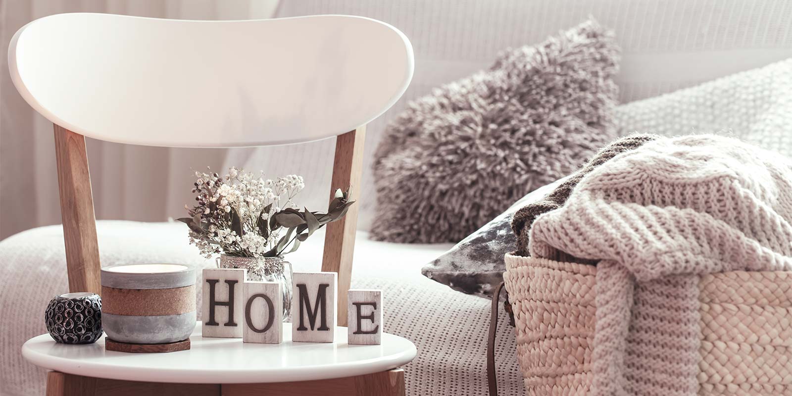 Encuadre de sala de estar minimalista con sofá y silla decorados con almohadones, velas y un juego de cubos de madera que forman la palara "HOME". En esencia de lo importante que es preparar la vivienda para mostrar las posibilidades que tiene.