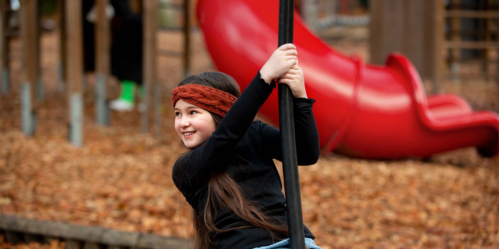 Imagen de niña con outfit otoñal jugando en un parque todo cubierto por hojas marrones de árbol. En representación de la estación de Otoño como otra de las estaciones favoritas para la inversión inmobiliaria.