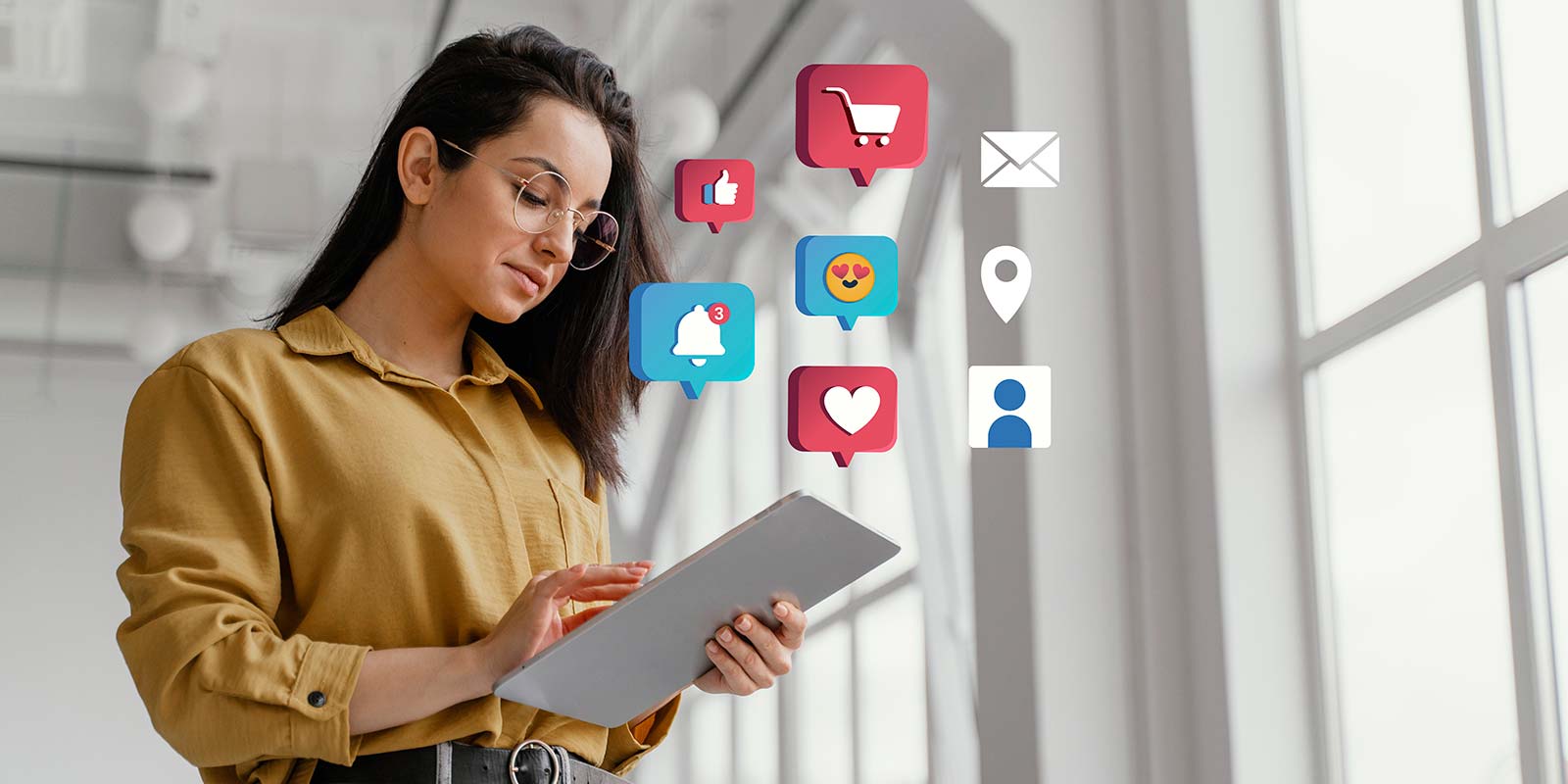 Mujer joven con una tablet en la oficina e íconos de reacciones de redes sociales flotando en el aire, en un estudio moderno y minimalista. En representación del trabajo del marketing en las estaciones del año y los momentos adecuados para realizar las ofertas inmobiliarias oportunas.