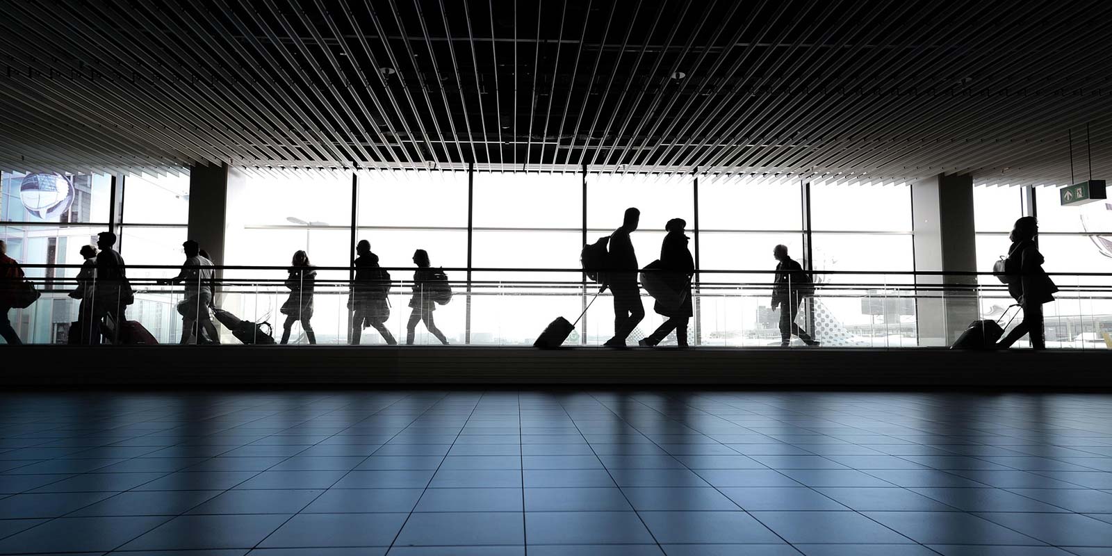 Foto de personas a contraluz yendo y viniendo en un aeropuerto. En concepto de los extranjeros que visitan la Costa del Sol y su tendencia a invertir en inmuebles como segunda vivienda o como inversión pasiva vacacional.