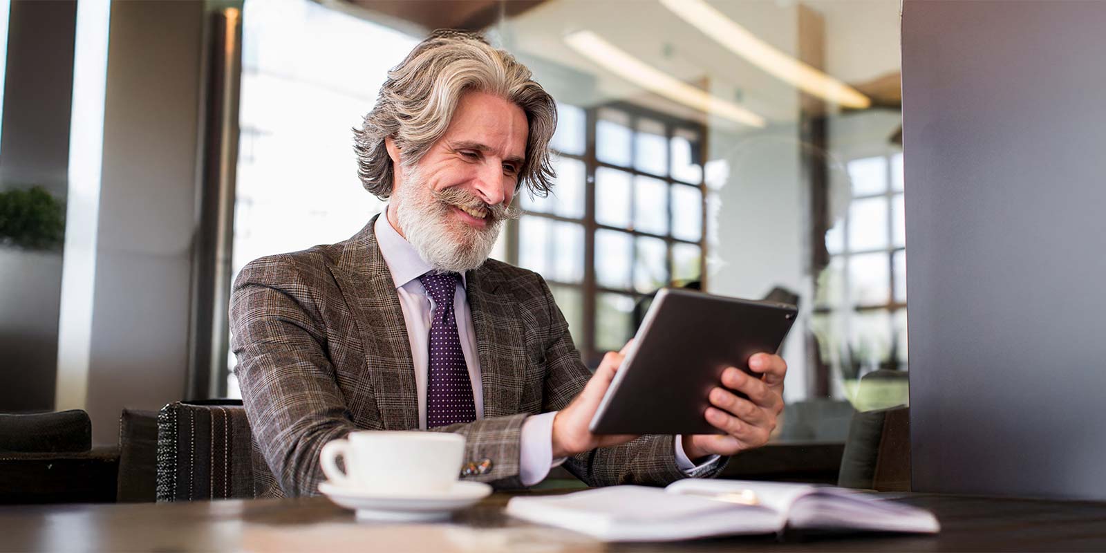 Hombre adulto en un café revisando una tablet, sentado en una mesa tomando un café. En referencia y personificación de un extranjero británico como uno de los principales turistas interesados en invertir en la Costa del Sol en sus pisos, casas, playas, municipios.