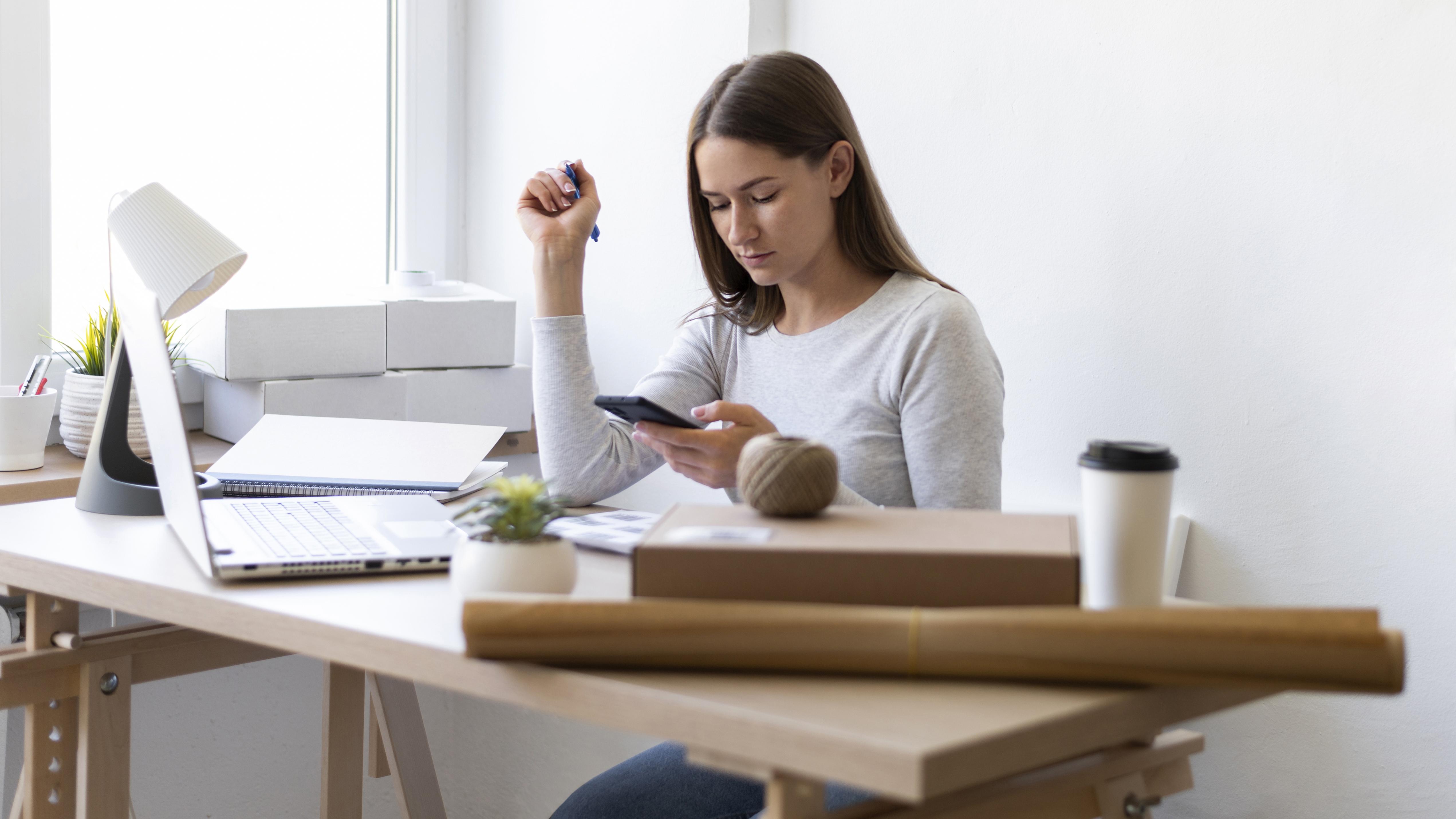 Mujer joven trabajando en escritorio con su ordenador y su móvil. En concepto del trabajo en el marketing digital y redes sociales como inversión a la hora de promover los inmuebles en la Costa del Sol