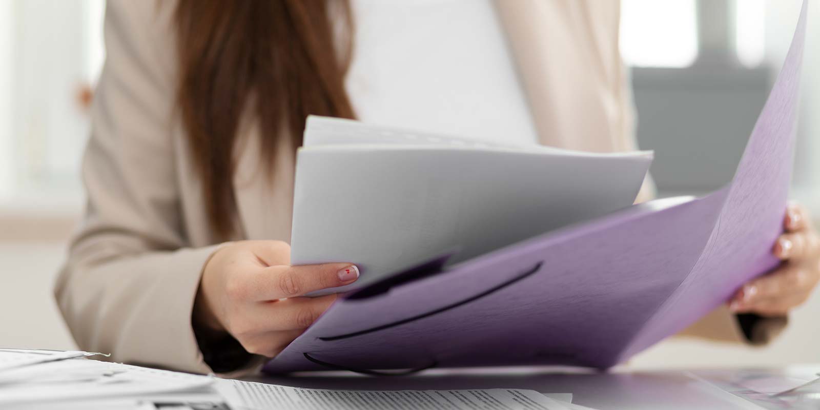 Imagen del torso de una mujer sosteniendo folios y carpetas. En referencia al revisar la documentación para que todo esté en orden legal y técnicamente a la hora de una operación inmobiliaria.