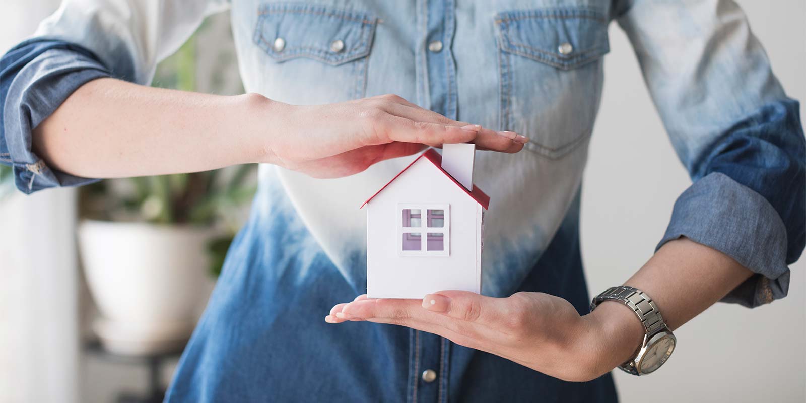 Imagen de sección media de una mujer que protege el modelo de una casa con sus manos. En referencia al tema sobre los seguros para el inmueble que debería contratar un inversor.