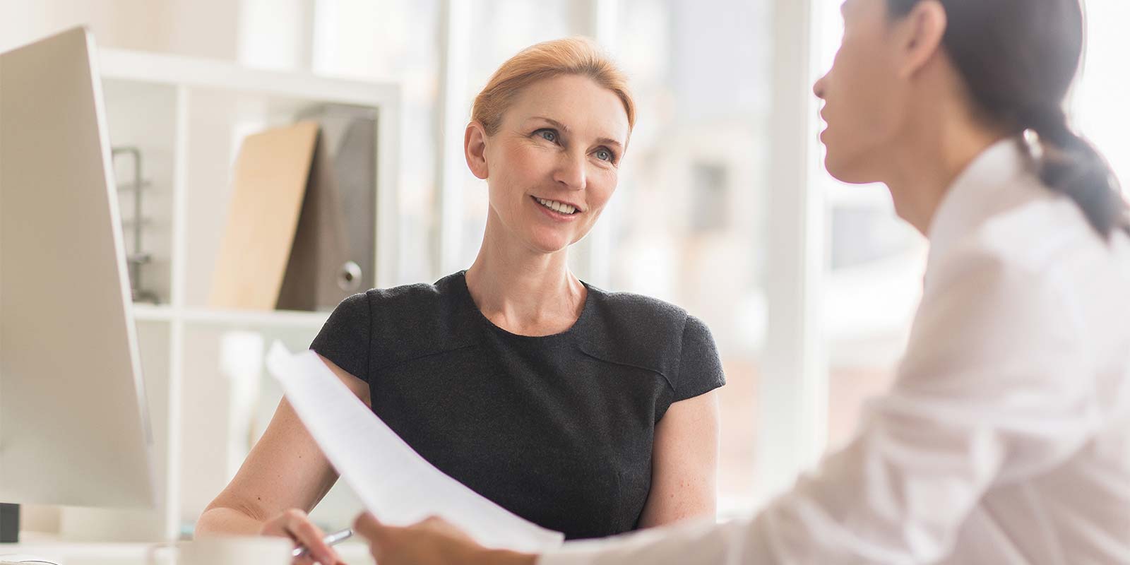 Dos mujeres reunidas en un estudio. En referencia a la profesional en inmobiliaria que con su conocimiento y experiencia transmite confianza y transparencia a sus clientes.