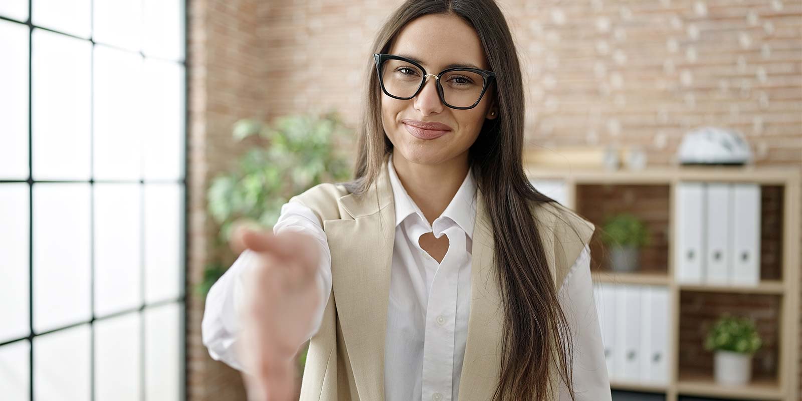 Mujer joven con gafas estirando la mano buscando estrecharla. En referencia a la tranquilidad y confianza que un agente inmobiliario le da a su cliente en la Costa del Sol